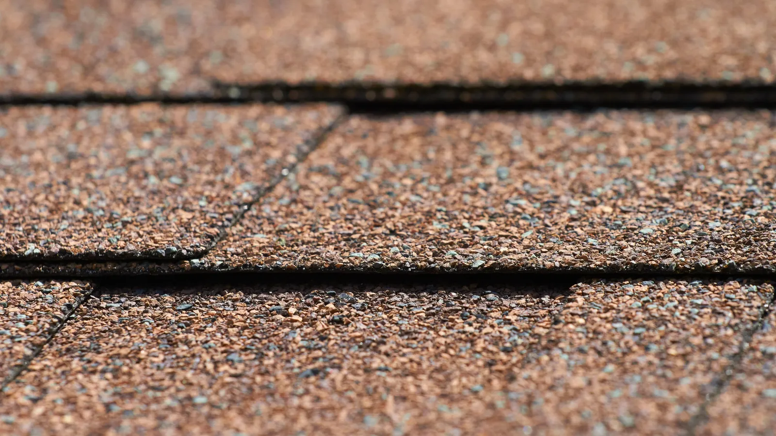 Brown asphalt shingle granules and overlapping tab edges in macro view