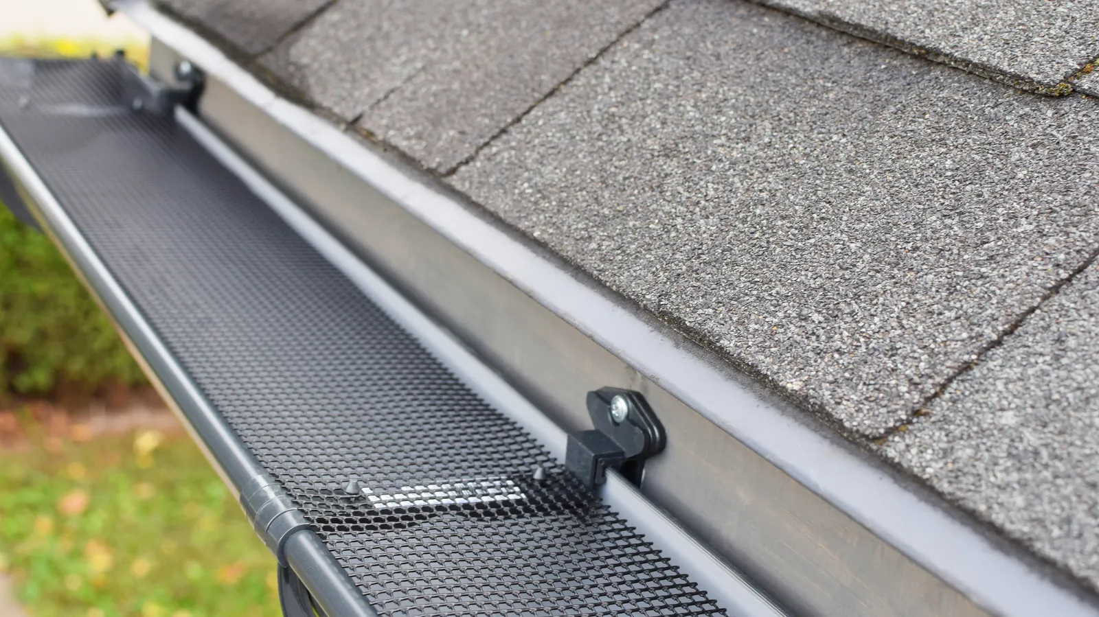 Gray asphalt shingles beside a gutter with mesh guard clipped over it
